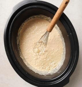Whisking milk and cheeses in a slow cooker.