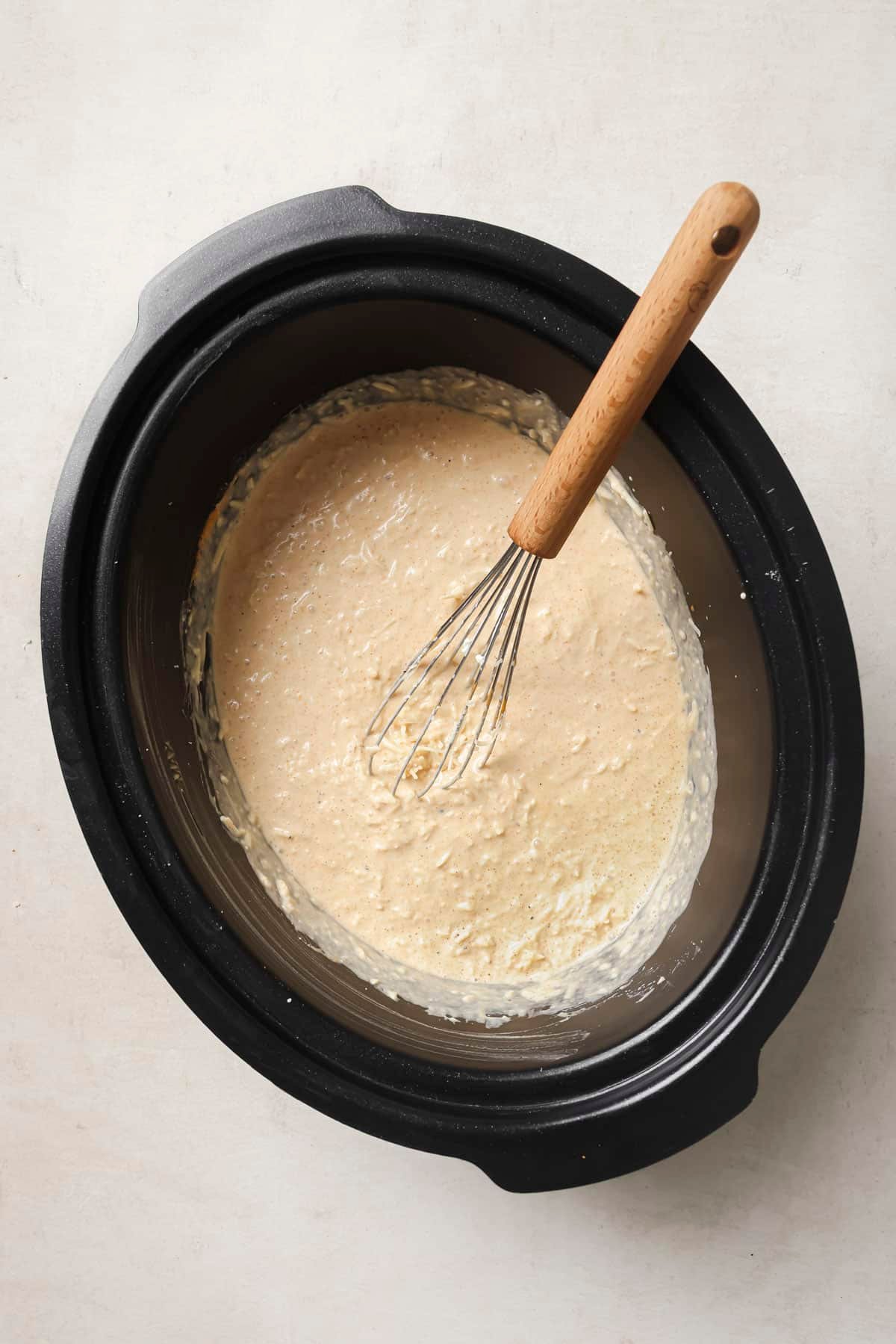 Whisking milk and cheeses in a slow cooker.