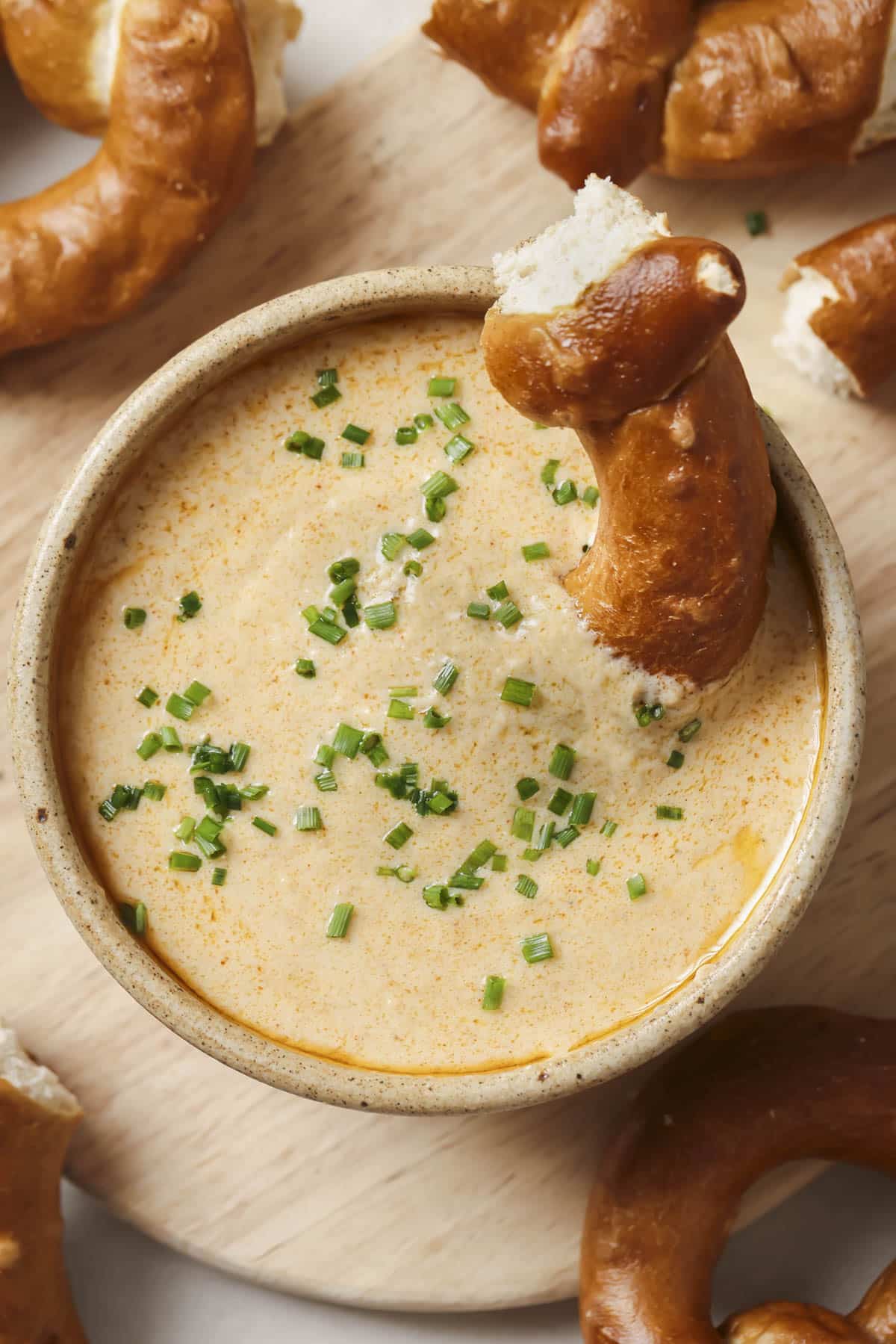 A pretzel dipped into a bowl of beer cheese dip.