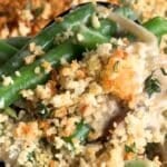Close-up of a scoop of creamy green bean casserole topped with a golden, crispy Parmesan–panko breadcrumb crust, showing bright green beans and fresh thyme.