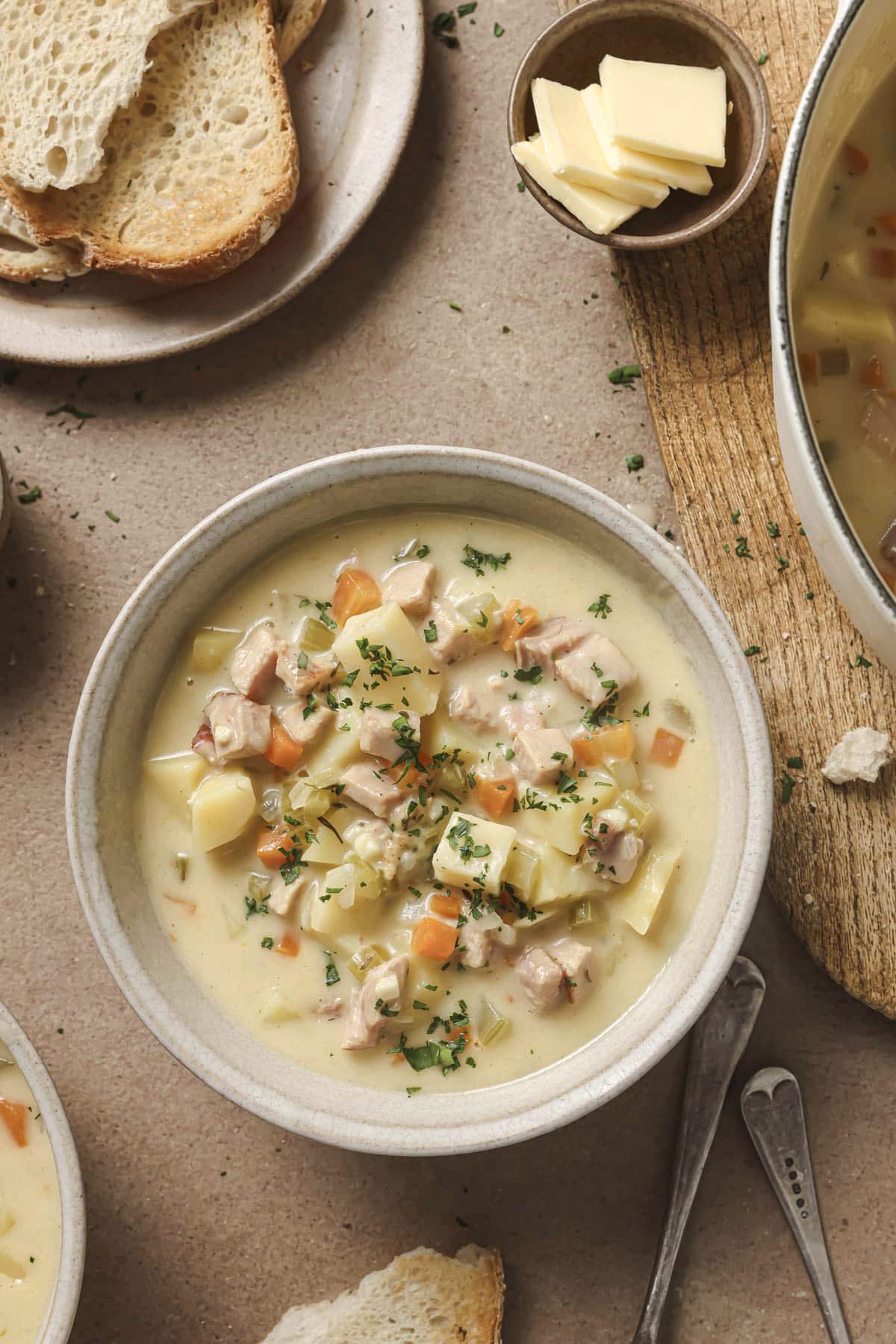 Ham and potato soup served in a bowl near a plate of bread and butter.