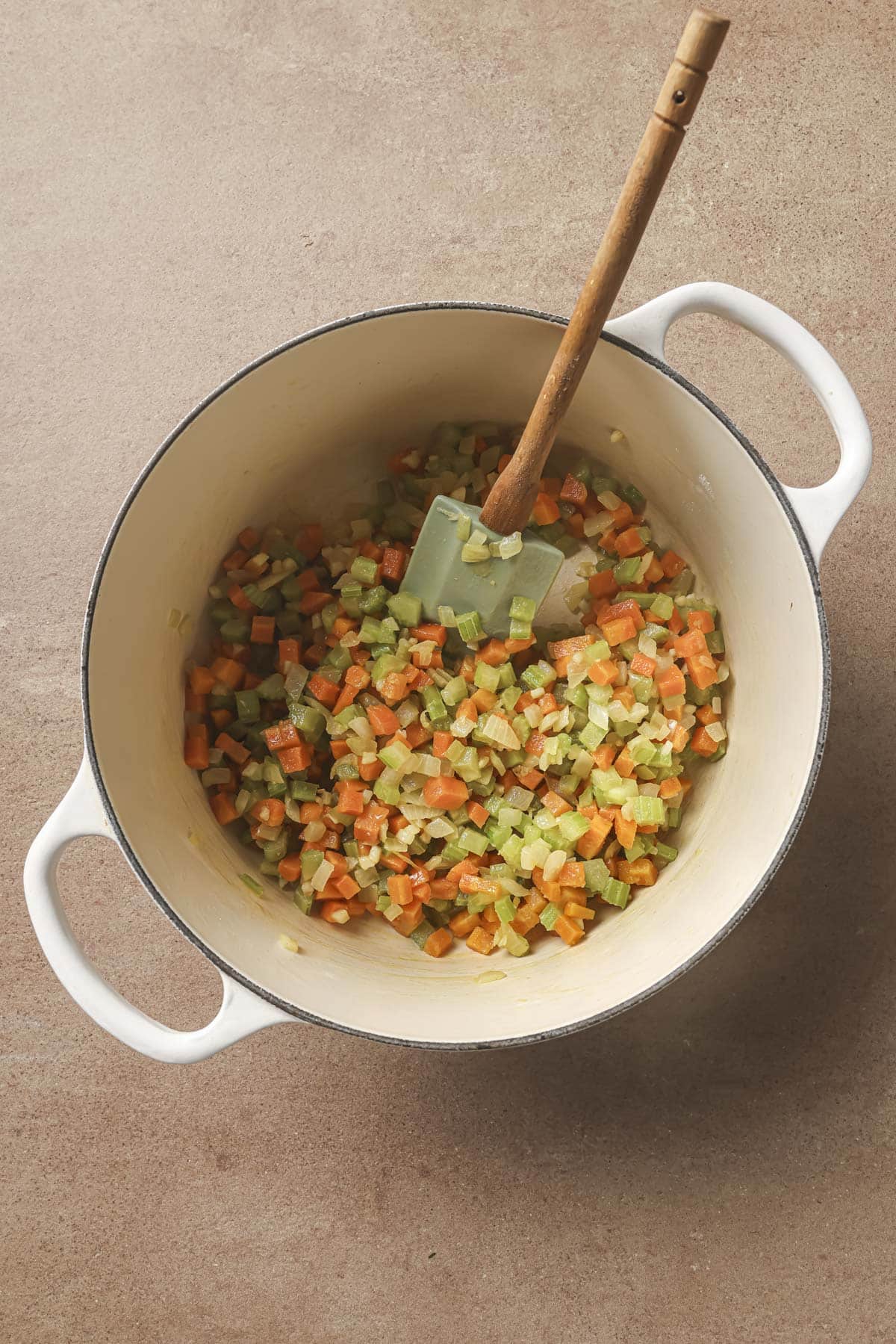 Using a spatula to stir flour into diced onions, carrots and celery.