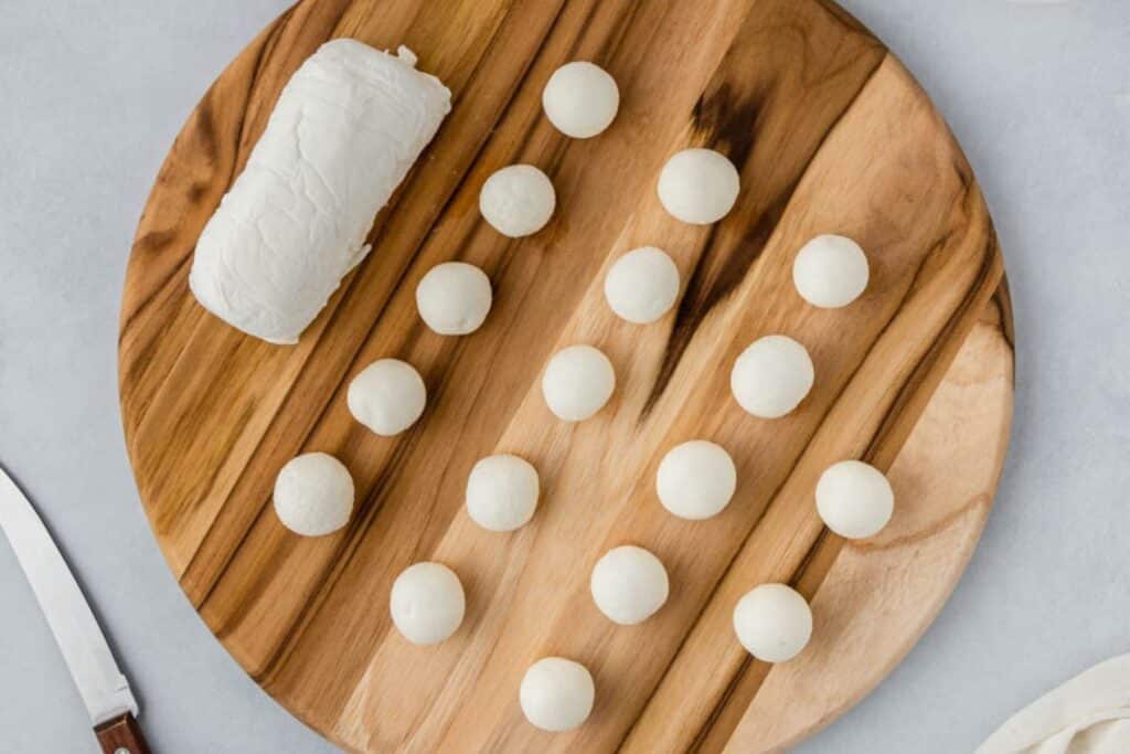 Balls of goat cheese on a wooden cutting board.
