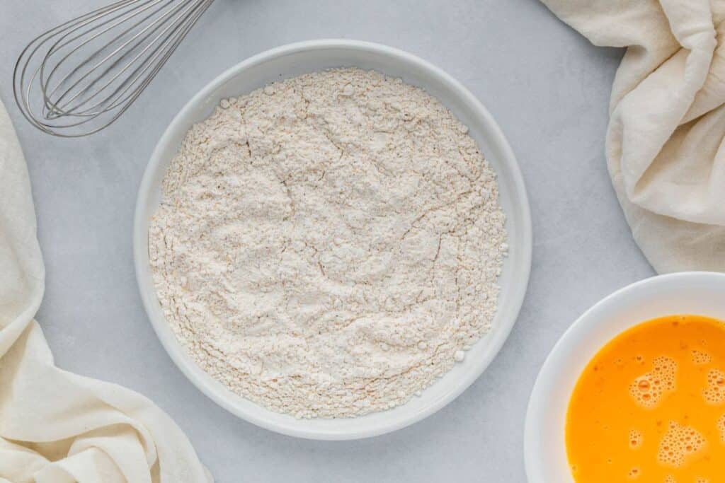 A dish of flour next to a dish of beaten egg.
