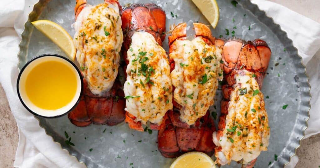 Air fryer lobster tail on a metal tray served with melted butter and lemon wedges.