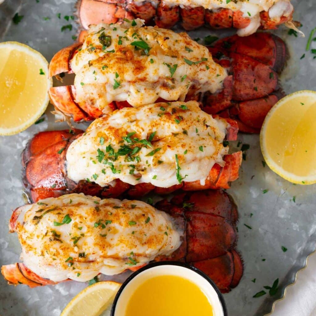 Air fryer lobster tail on a metal tray served with melted butter and lemon wedges.