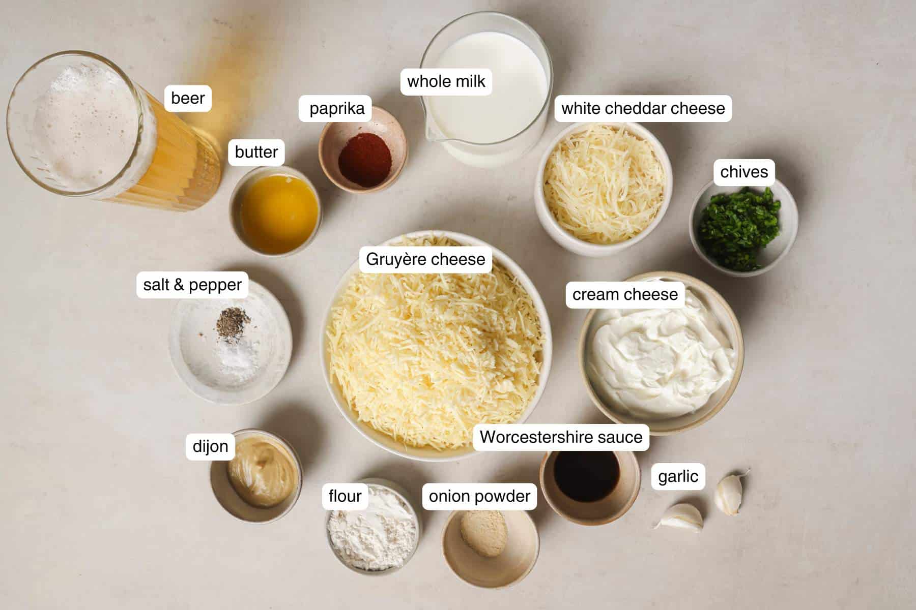 Glass of beer near bowls of cheese, spices, butter, and milk.