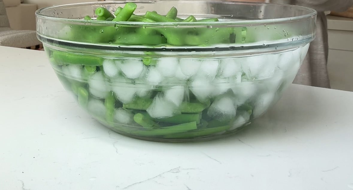 Green beans in a glass bowl of ice water.