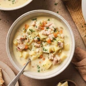 Two bowls filled with ham and potato soup with a spoon in one.