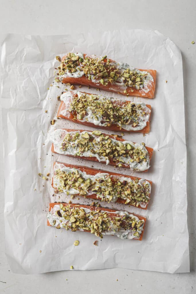 Uncooked salmon topped with mayo mixture and chopped pistachios.