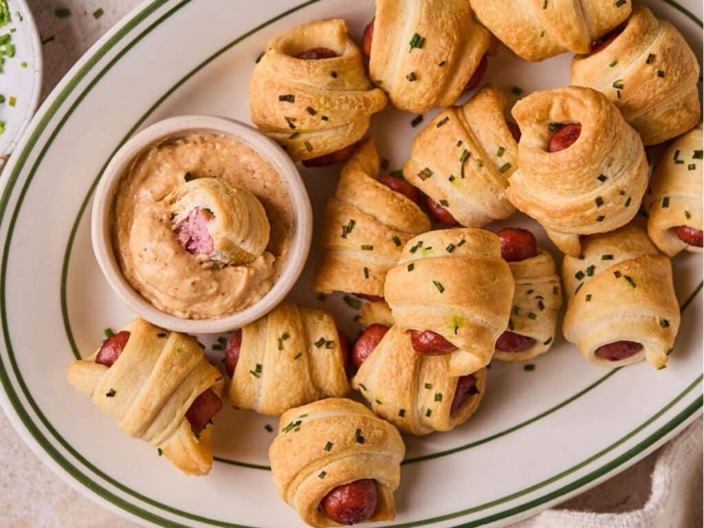 A plate full of air fryer pigs in a blanket with a side of homemade queso dip.