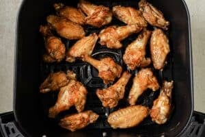 Chicken wings covered in sauce in the air fryer basket.