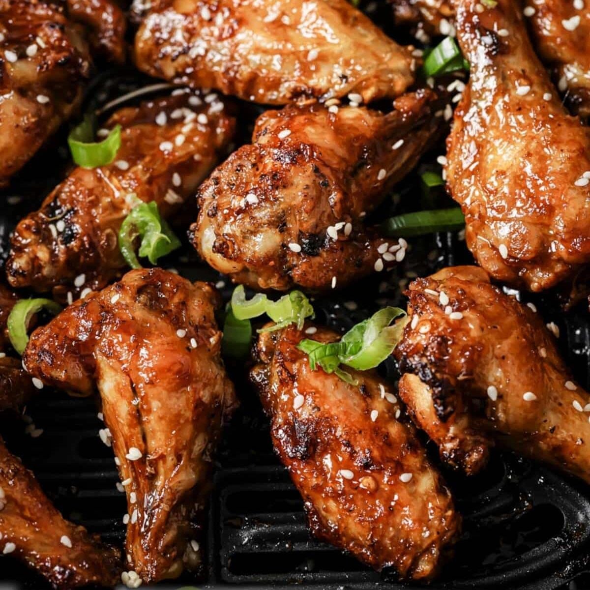 Asian wings in the air fryer basket, garnished with sesame seeds and green onions.