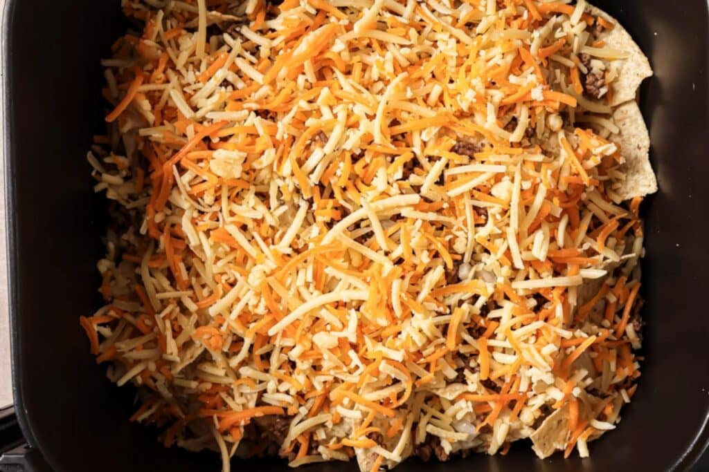 Adding cheese on top of tortilla chips.