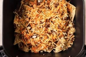 Adding cheese and beef to tortilla chips.