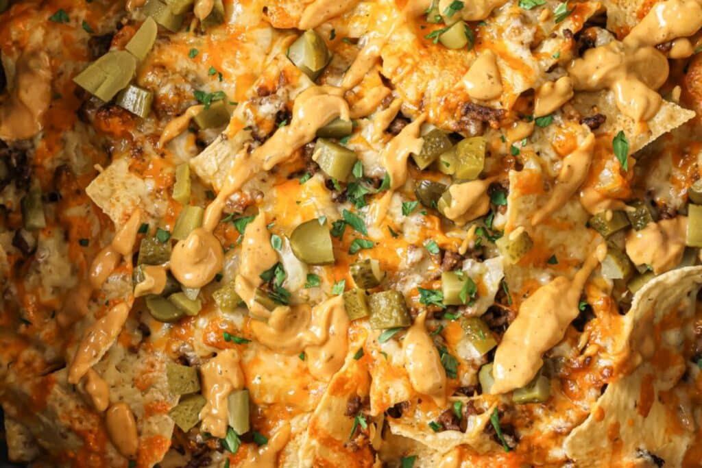 Adding burger sauce and pickles to nachos.