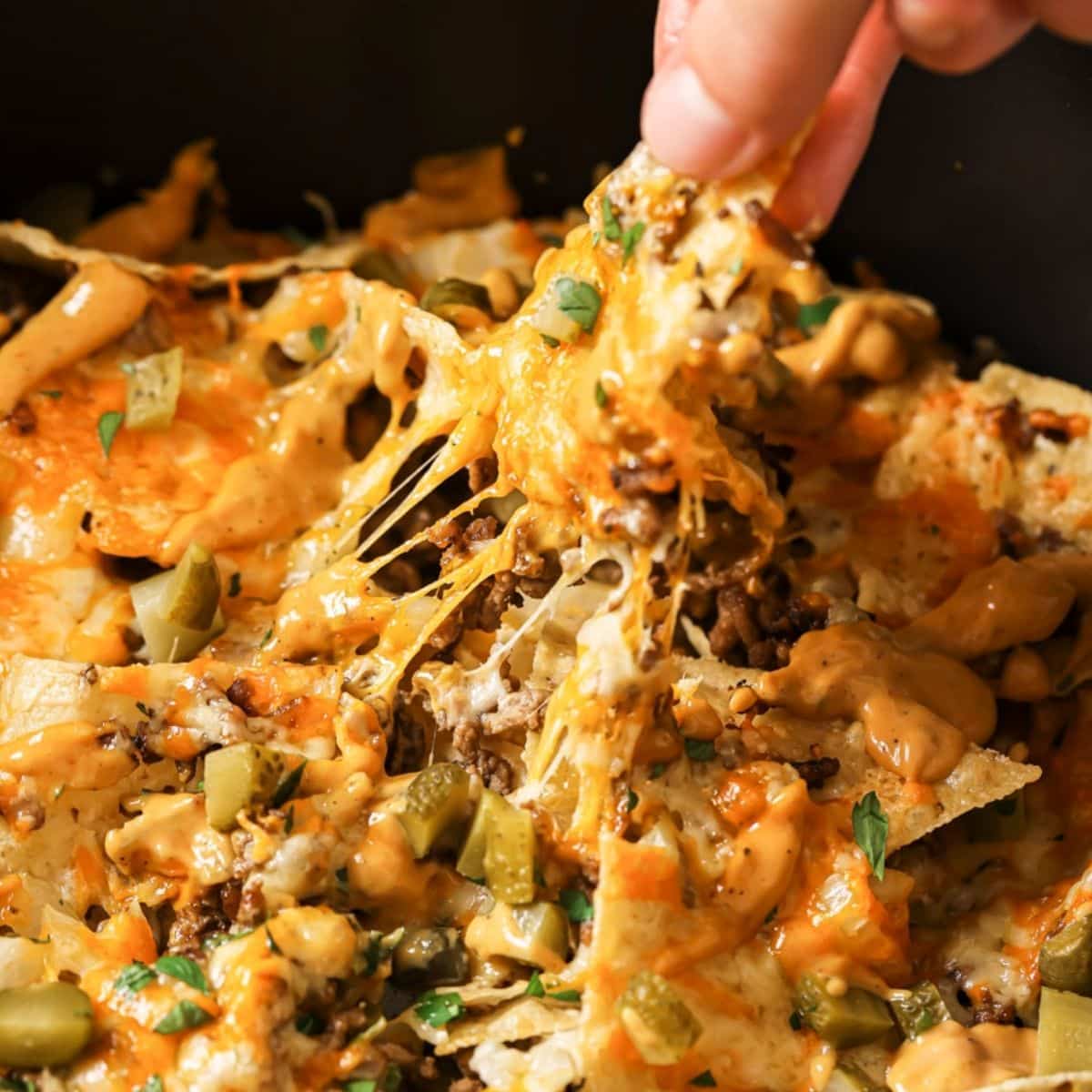 A hand taking a chip from a plate of air fryer nachos.