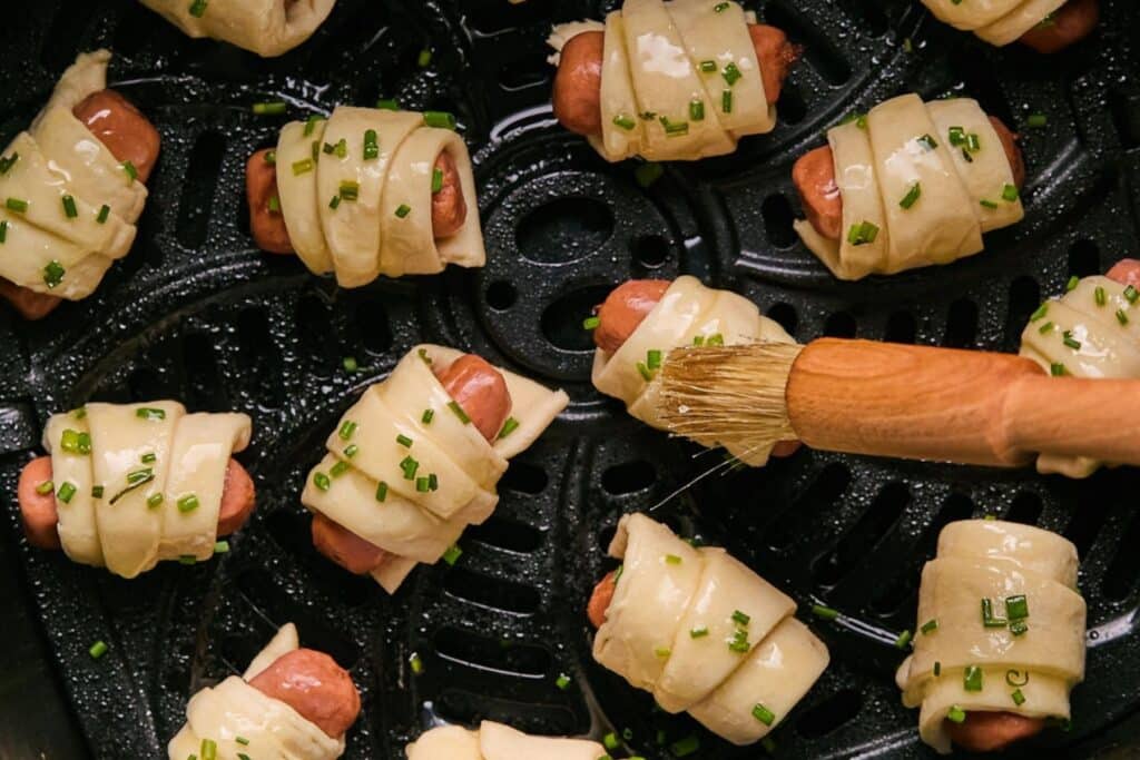 Brushing uncooked pigs in a blanket with melted butter.