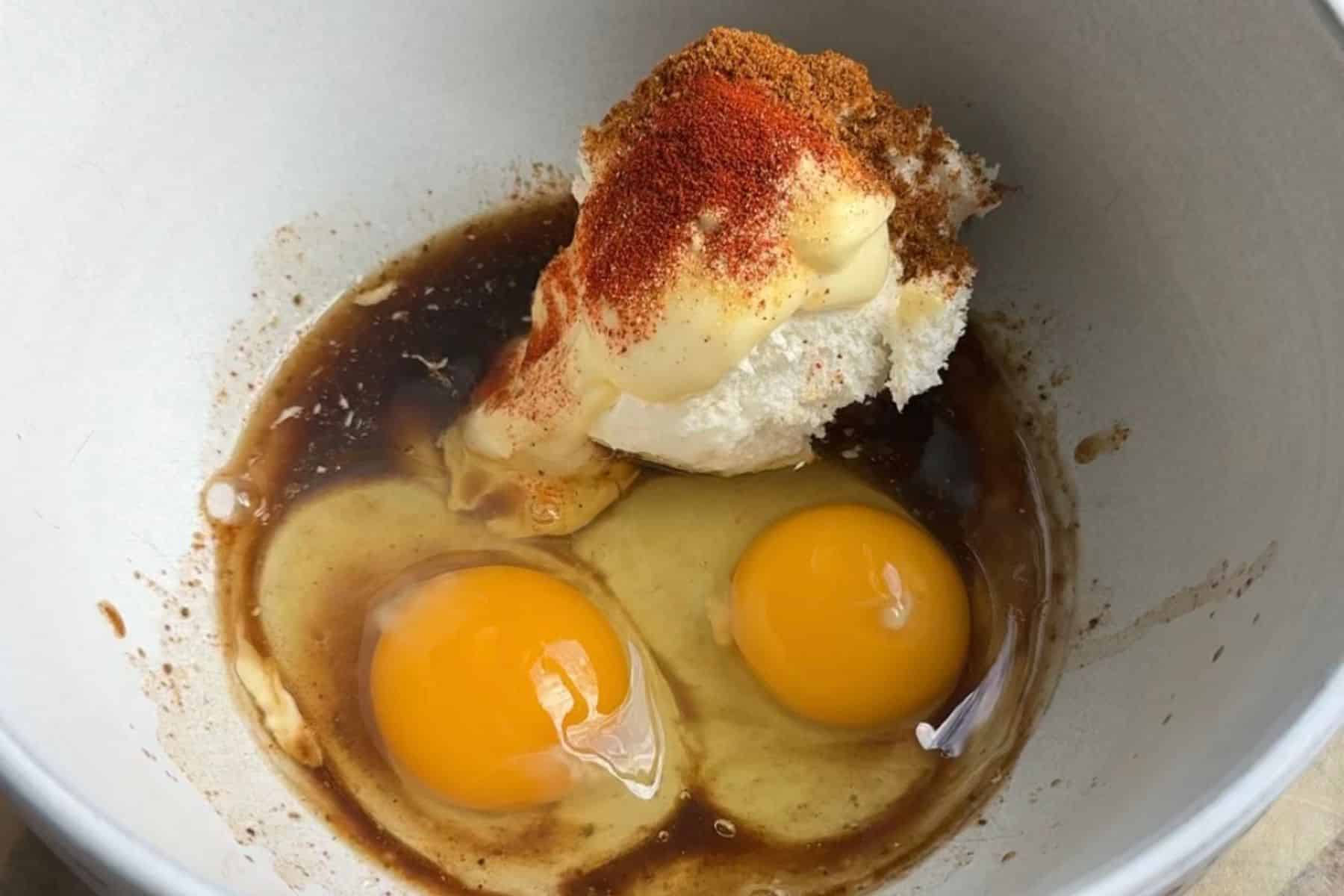 Two eggs, mayonnaise, and spices in a white bowl.