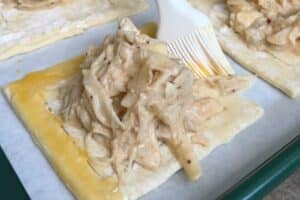 Using a silicone pastry brush to add egg wash to the sides of a pastry square.