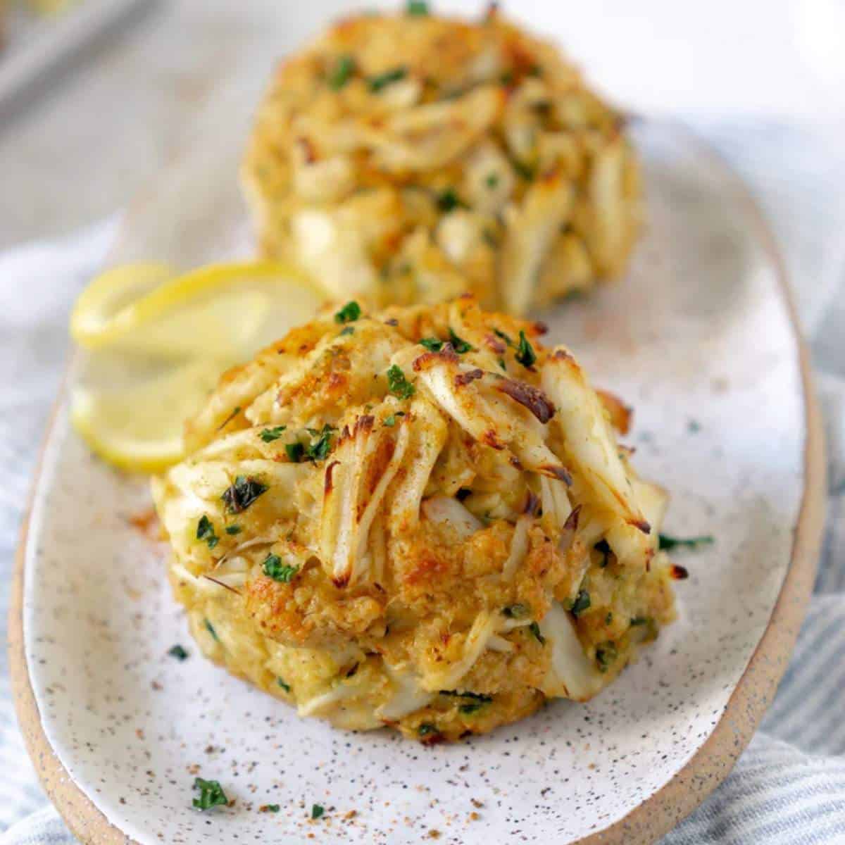 Two Maryland Crab cakes on a plate with slices of lemon.