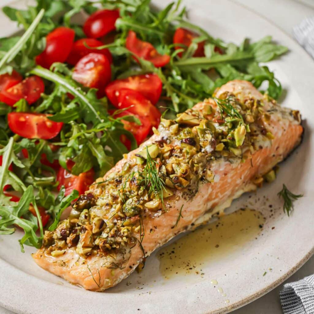 Pistachio crusted salmon served alongside a green salad with tomatoes.