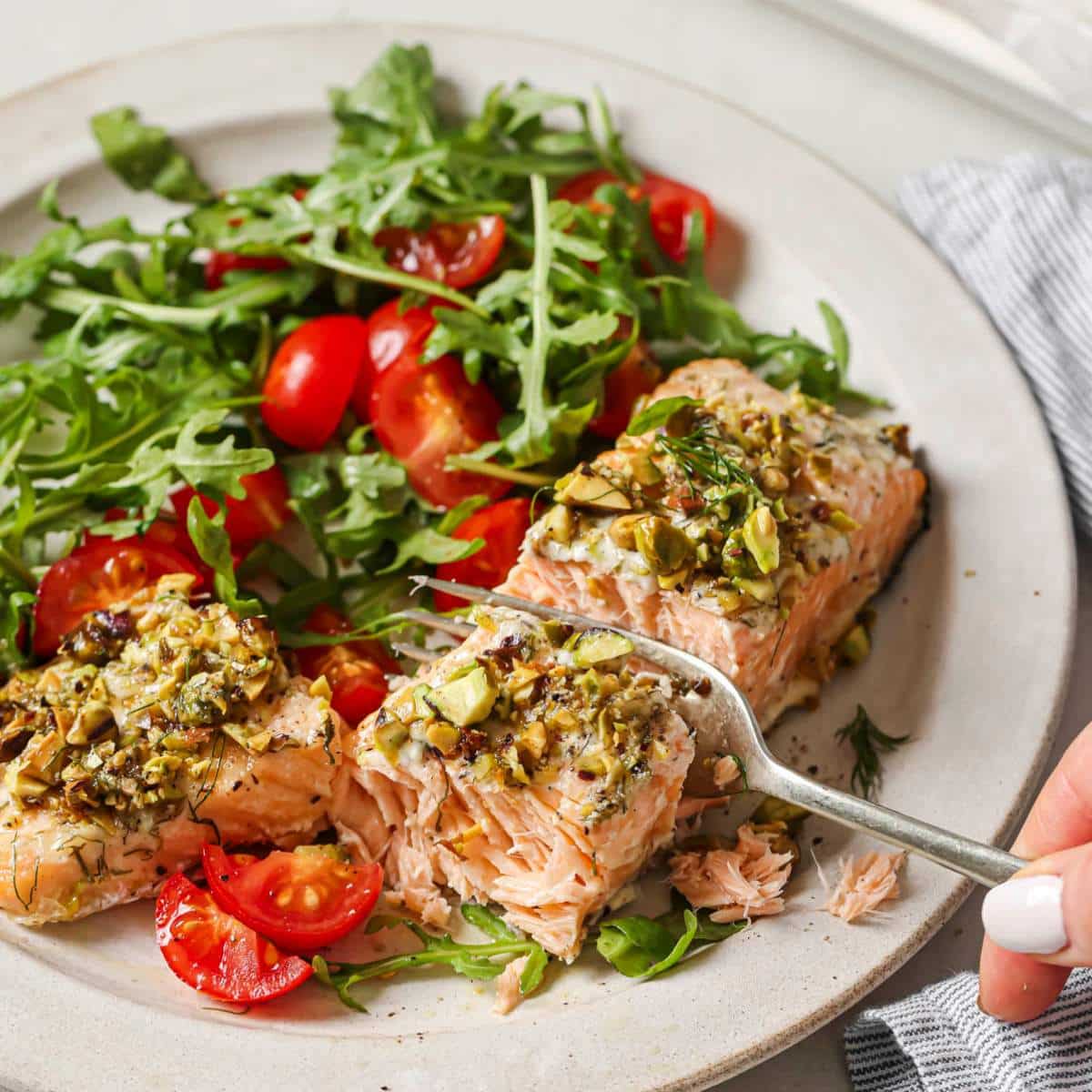 Using a fork to cut into a piece of salmon near a salad.