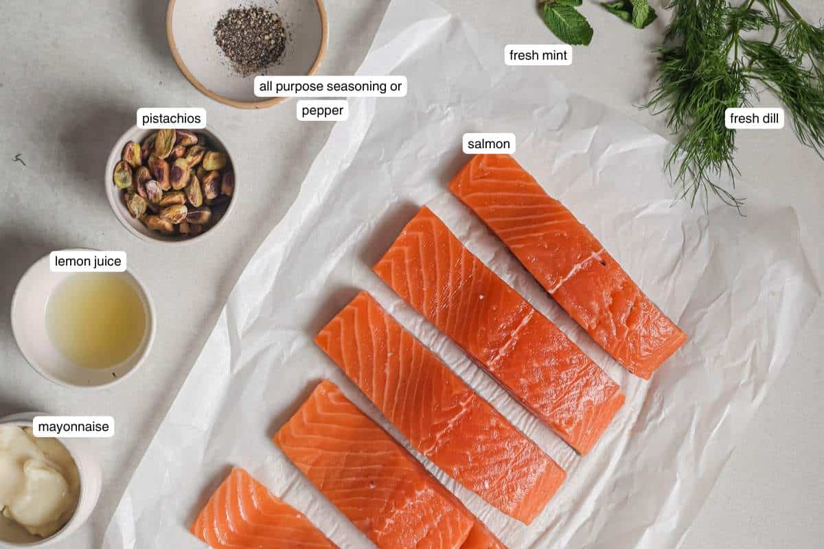 Uncooked salmon filets near small bowls with lemon juice, mayo, pistachios and pepper.