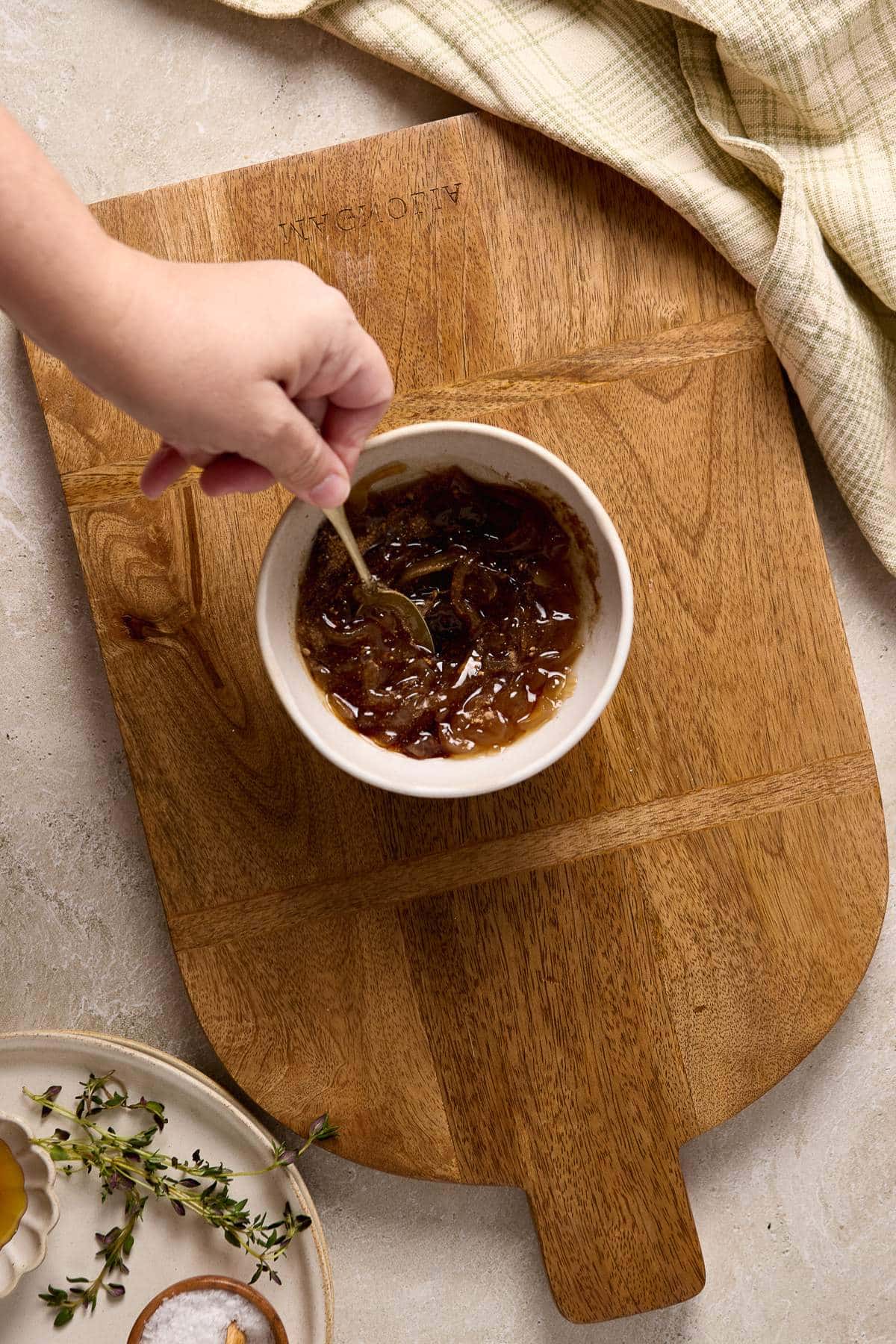 Stirring onion jam with seasonings in a small white bowl.