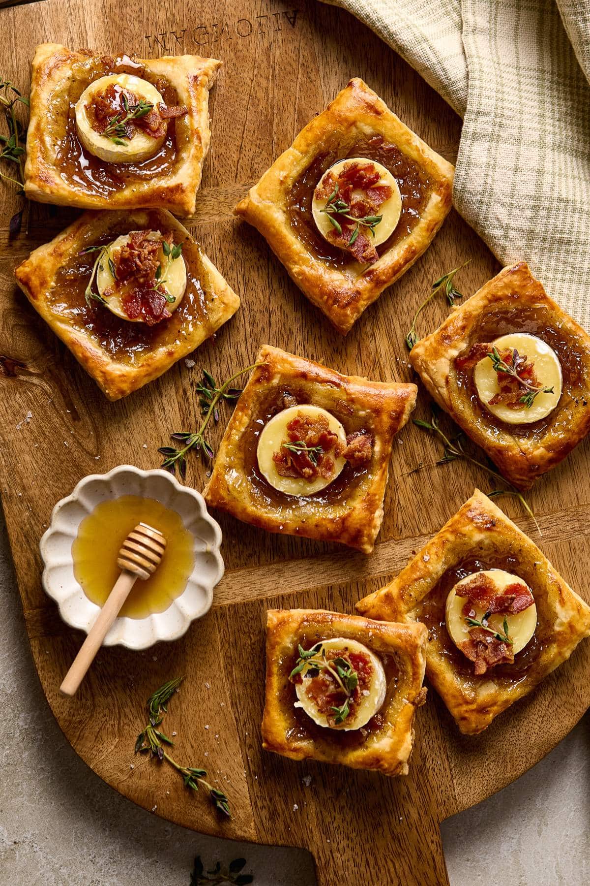 Puff pastry Brie Bites on a wooden cutting board near fresh thyme and honey.
