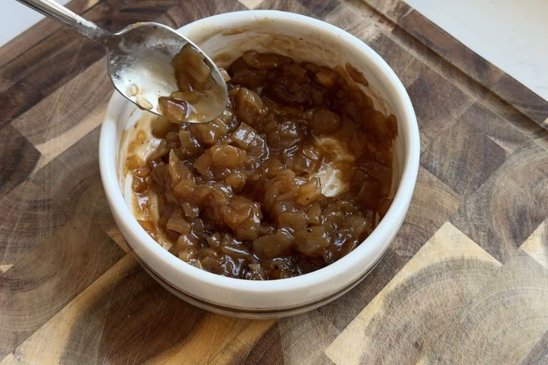 Stirring onion jam with seasonings in a small white bowl.