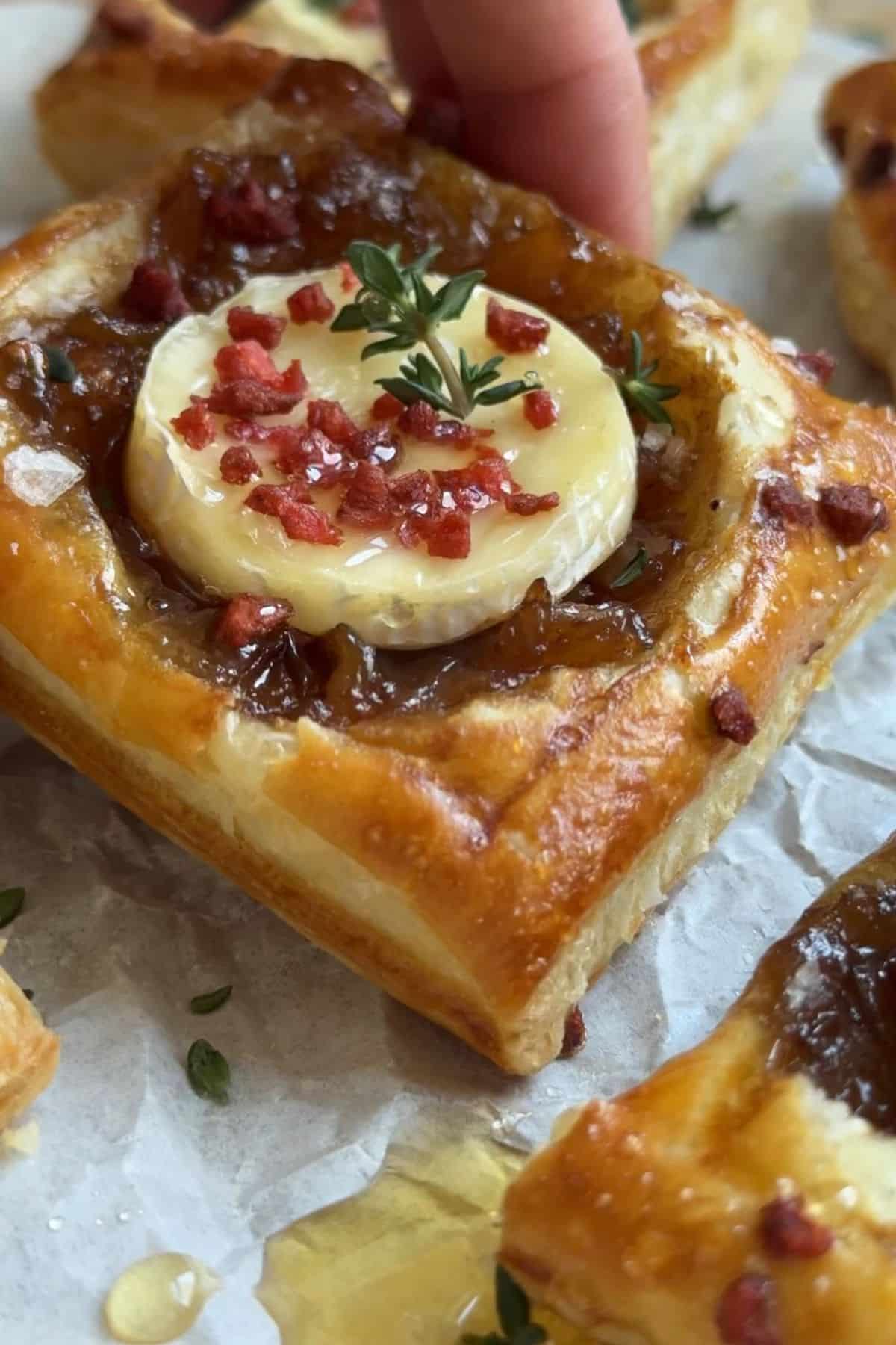 Hand holding a puff pastry tart filled with onion jam and brie.