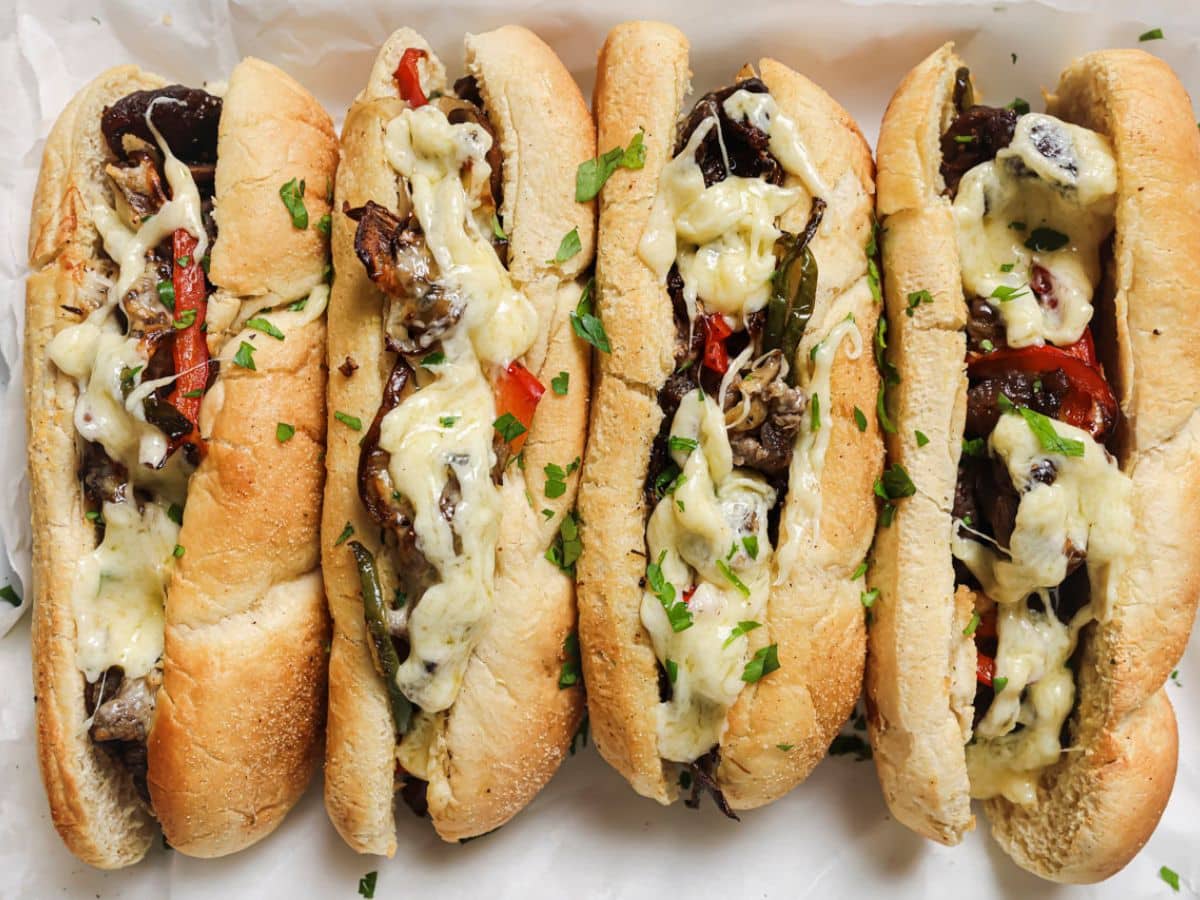 Several air fryer philly cheesesteak sandwiches on a platter lined with parchment.