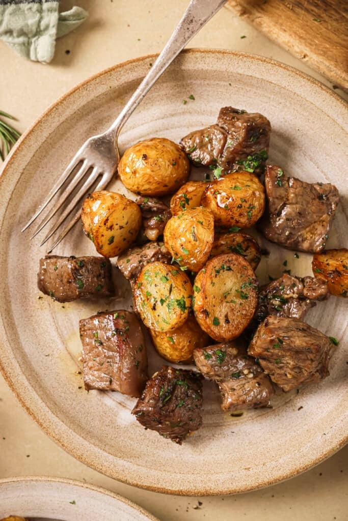 Air fried steak bites and potatoes on a white plate with a fork.