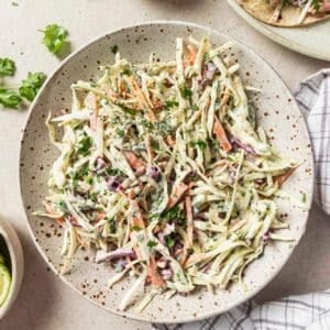 Fish taco slaw on a plate near a plate of fish tacos and freshly chopped cilantro.