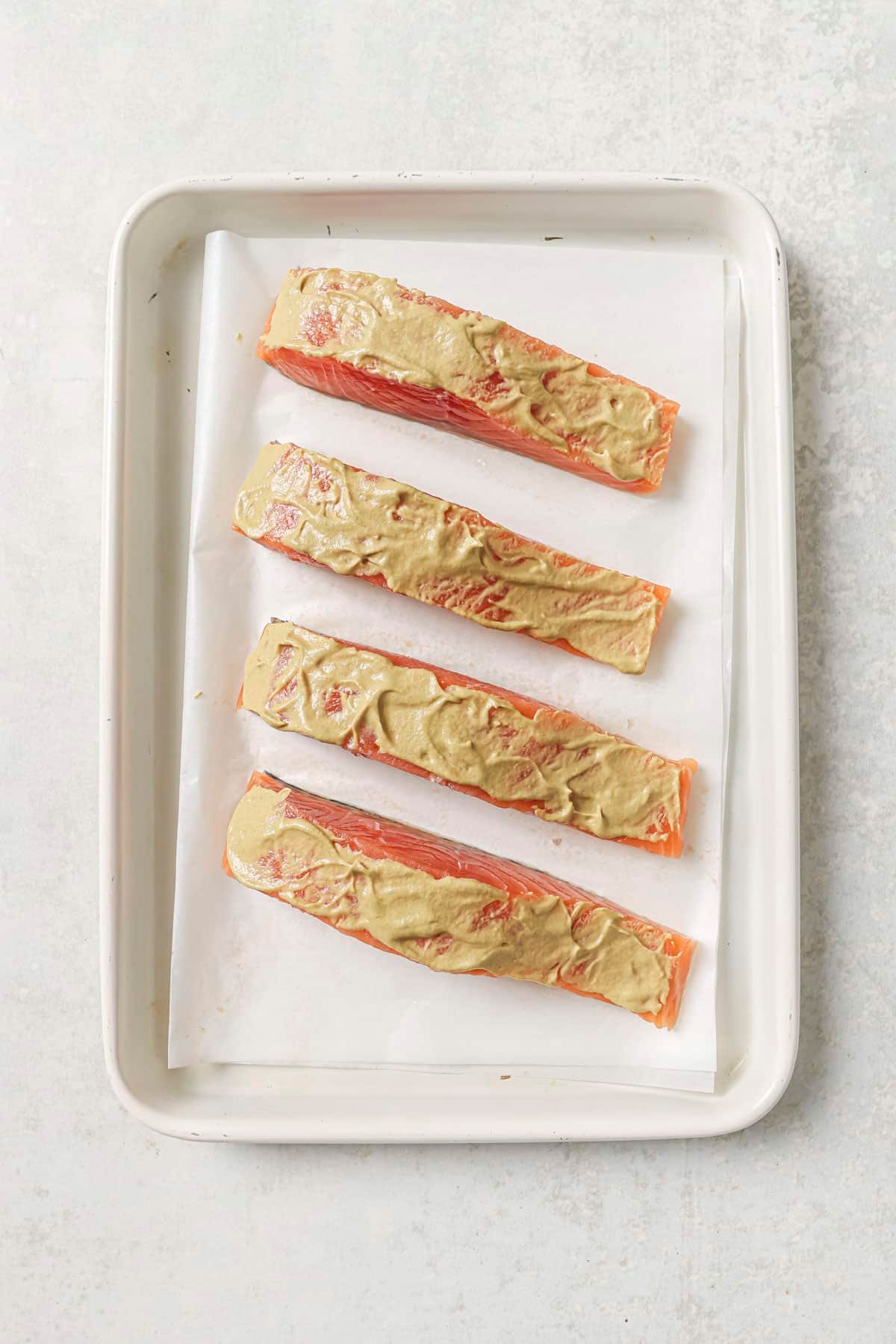 Dijon mustard spread over uncooked salmon on a pan.