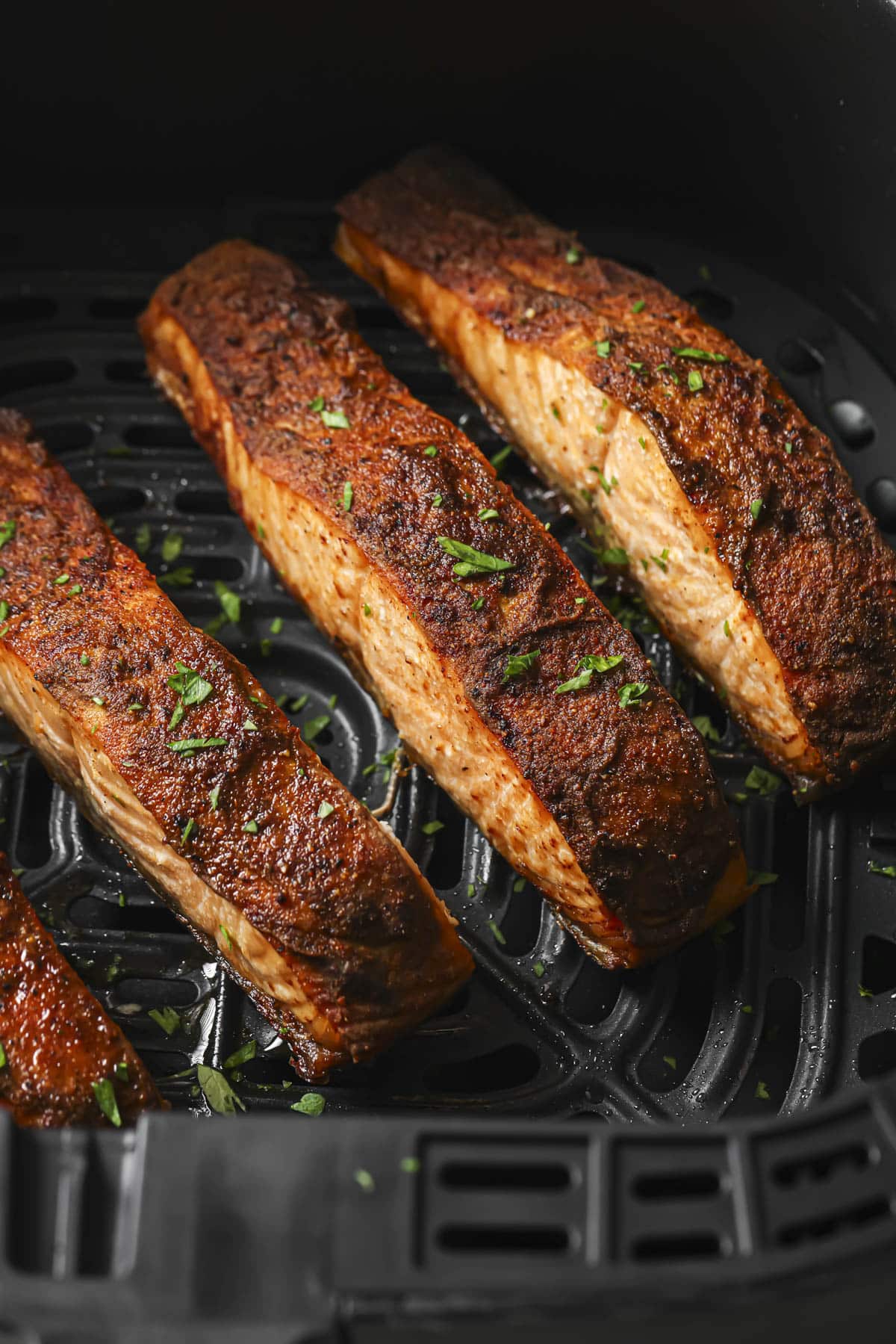 Salmon in an air fryer topped with fresh herbs.
