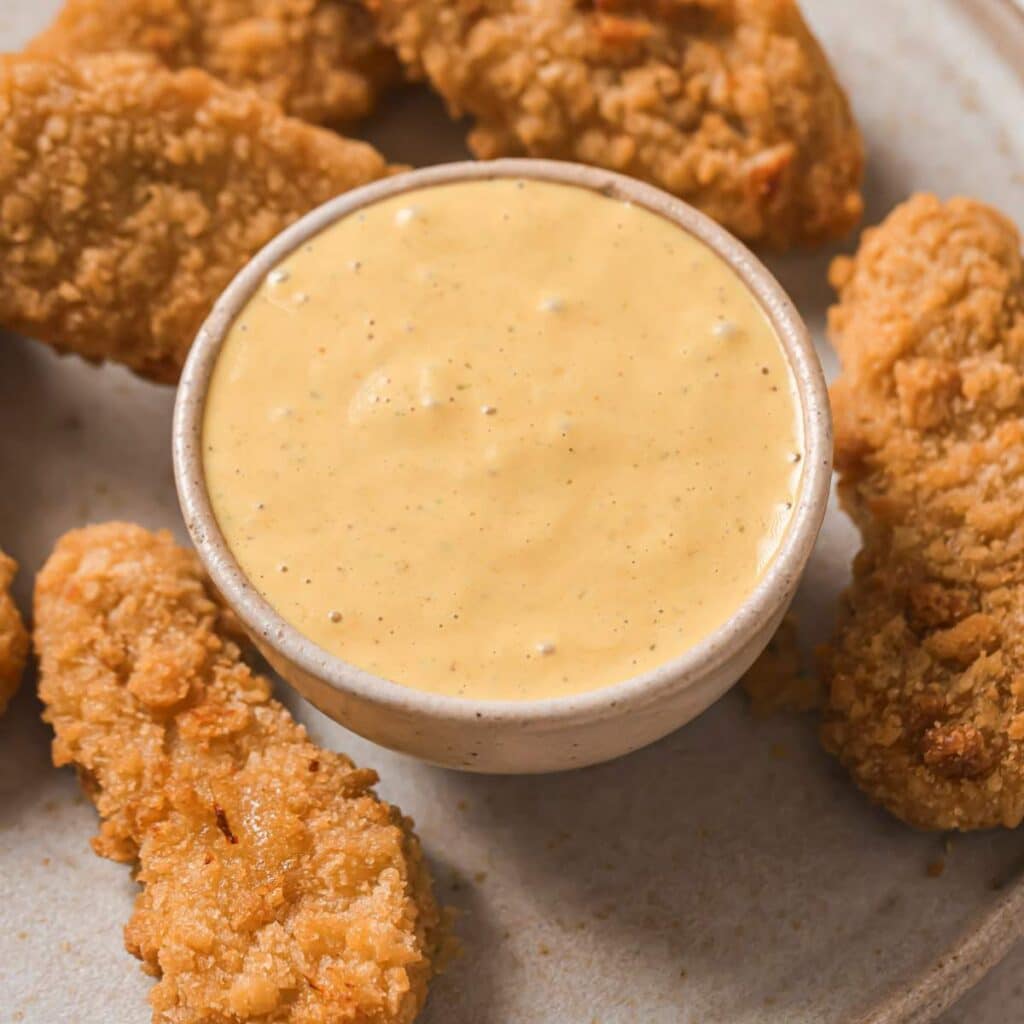 Chick-fil-A sauce in a bowl near chicken tenders on a plate.