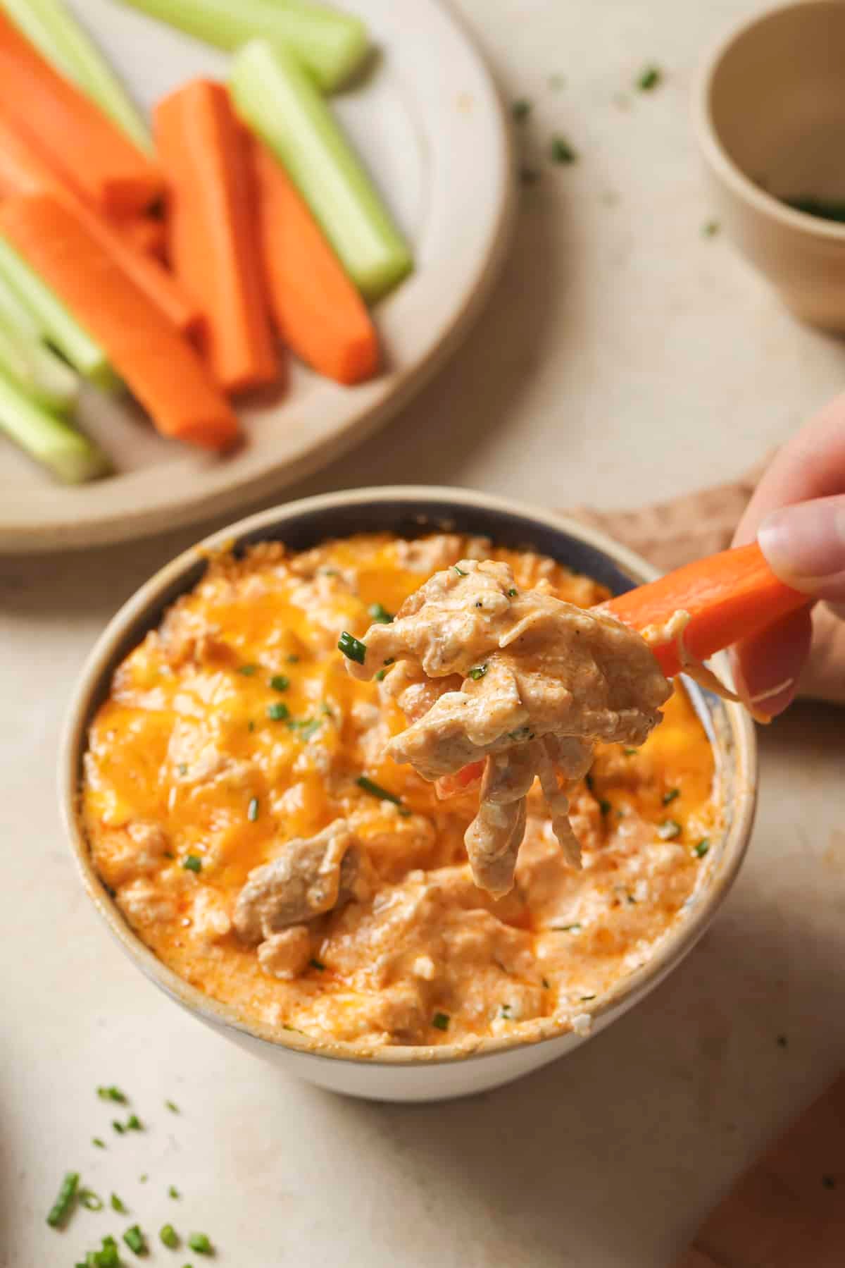 Dipping carrot stick into bowl of buffalo chicken dip.
