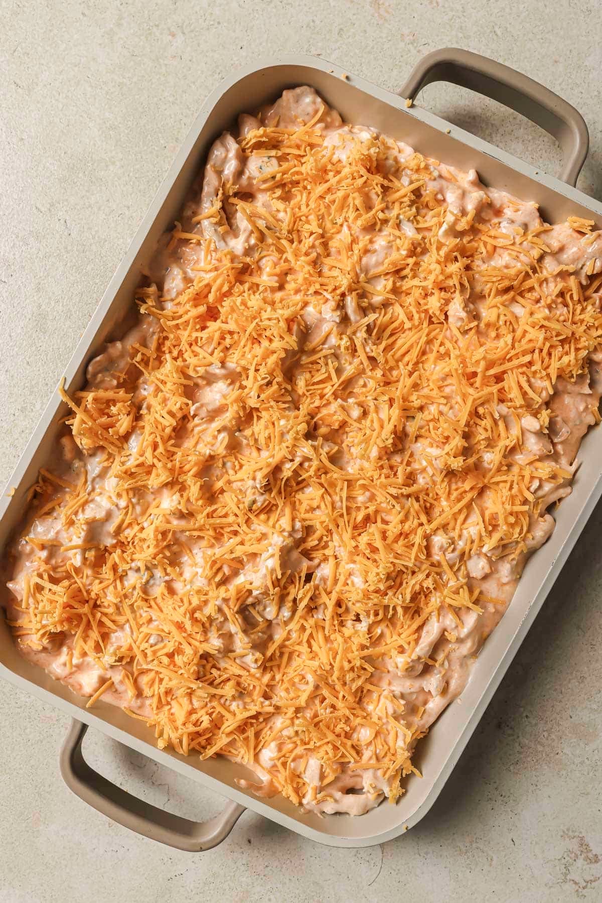 Buffalo chicken dip in a baking dish topped with shredded cheese.
