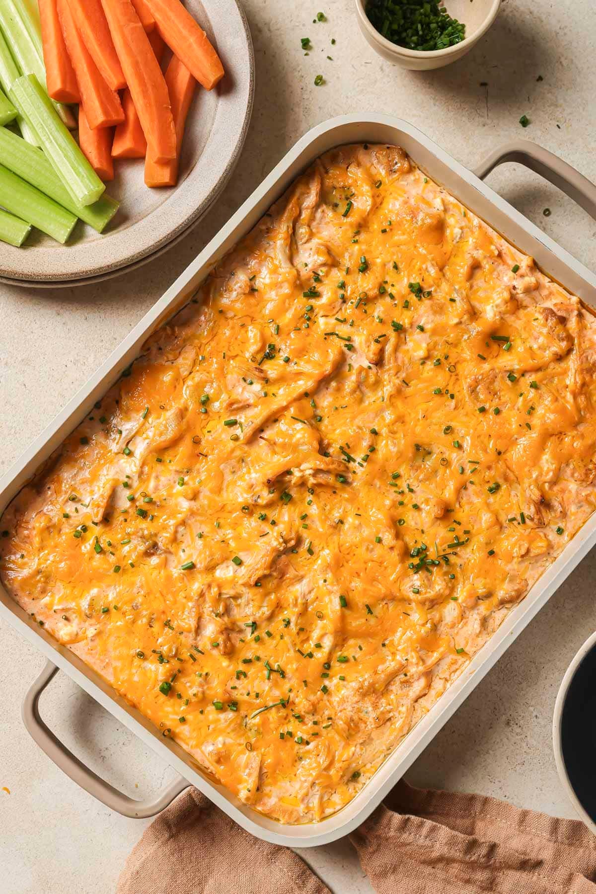 Baked healthy buffalo chicken dip served with freshly cut carrots and celery.