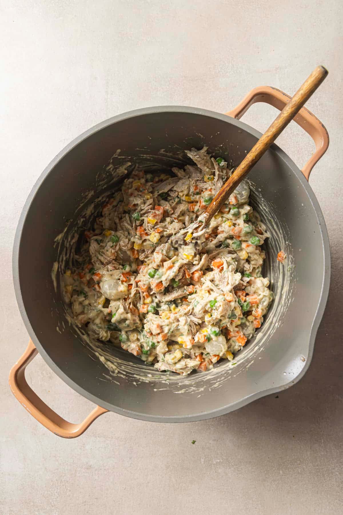 Stirring chicken and veggies with a creamy sauce in a pot.