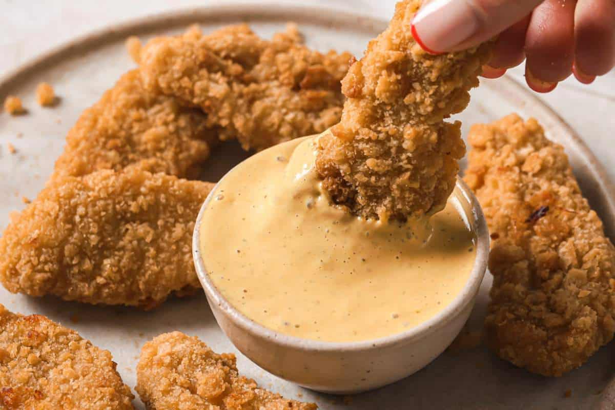 Dipping a chicken tender into a small bowl of Chick-fil-A sauce.
