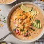 a bowl of creamy chicken fajita soup topped with tortilla chips, cilantro, and avocado in a white bowl with a spoon resting on the side
