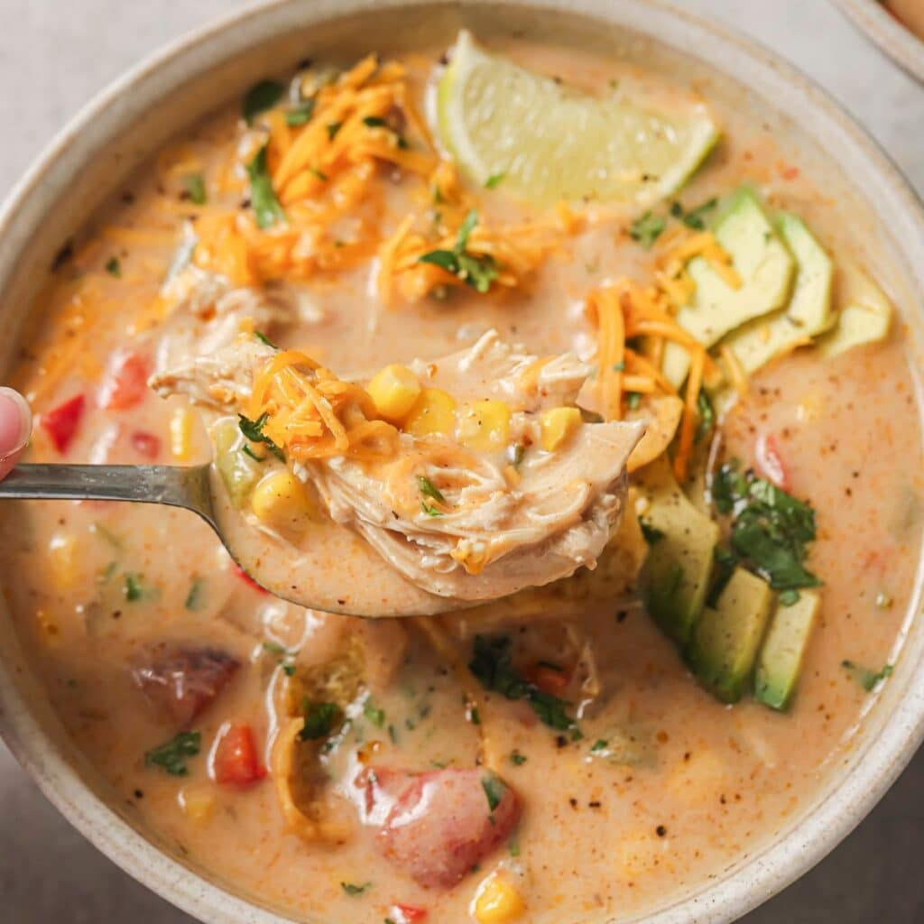 a close up of a spoonful of chicken fajita soup with a creamy broth, shredded chicken, and loaded with toppings. 
