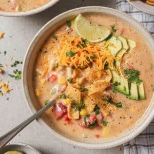 a bowl of creamy chicken fajita soup topped with tortilla chips, cilantro, and avocado in a white bowl with a spoon resting on the side