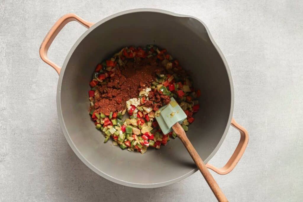 sauteeing peppers and onions in a soup pot with a spatula resting inside. 