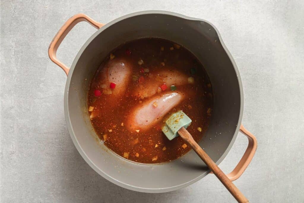 broth poured over raw chicken breasts in a soup pot with cooked peppers and onions to create the base of chicken fajita soup