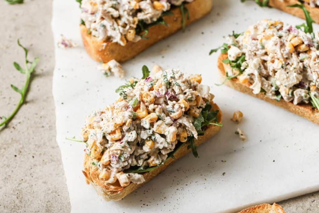 mexican street corn chicken salad atop a slice of sourdough bread on a white cutting board. 