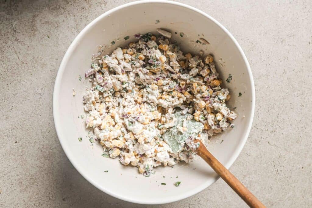 mixing the dressing into the street corn chicken salad ingredients until combined in a mixing bowl 